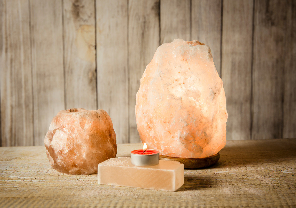 Hymalaian rock salt lamp turend on, salt candle holder with candle burning inside, bar of salt soap on wooden background.